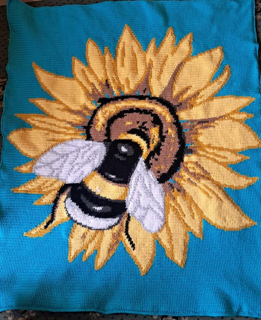 Embroidered design of a bee on a sunflower on a blue fabric background. Crocheted by Charlotte Nicole Lewis
