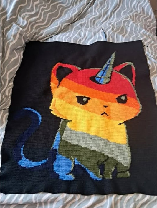 Crochet graphghan pillow with a cat wearing a unicorn horn on a bed.
Crocheted by Charlotte Nicole Lewis