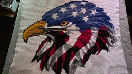 Crocheted blanket with an eagle design featuring the American flag on a bed. Design by Geeky Graphghans. Crochet by Martha Smith Atkins