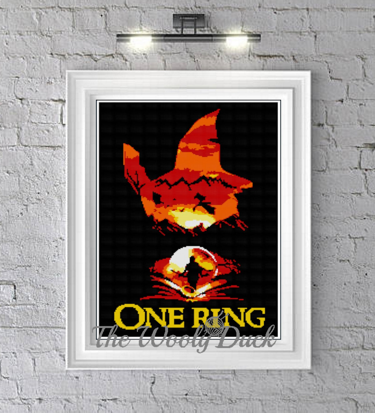 A graphghan pattern for 'One Ring' Hobbit inspired blanket, displayed in a frame with a brick wall background. The image shows the pattern for crochet or cross stitch, with a fantasy-themed graphic.
