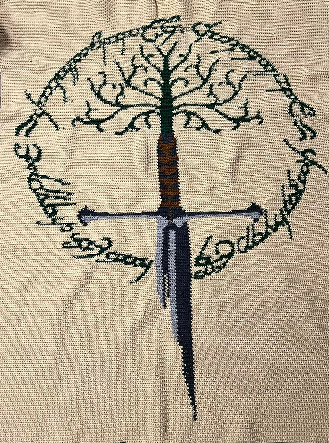 Blanket with embroidered design of a tree and sword on a wooden floor. NArsil crochet pattern