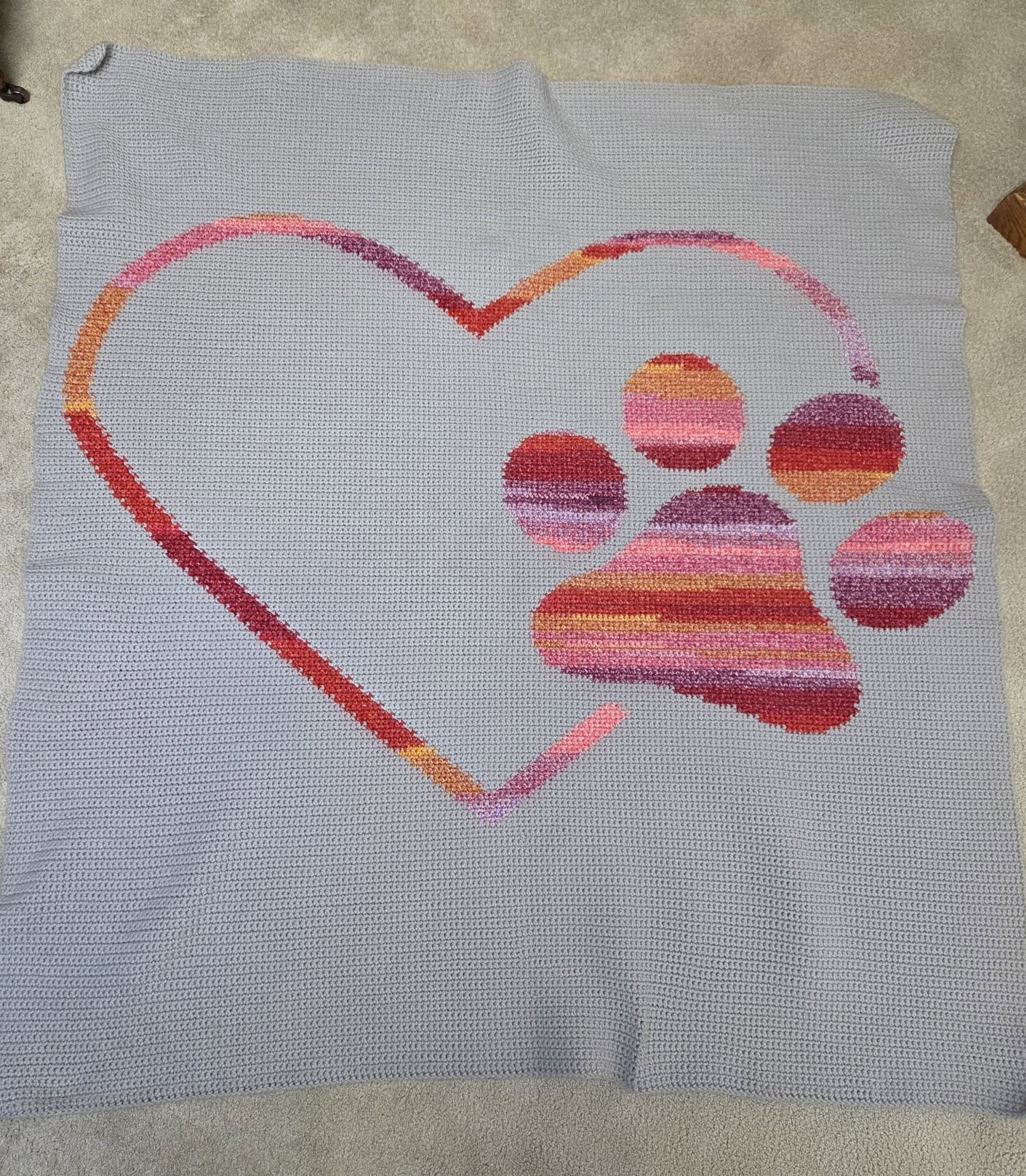 Cross-stitched design of a heart with a paw print on a gray fabric background