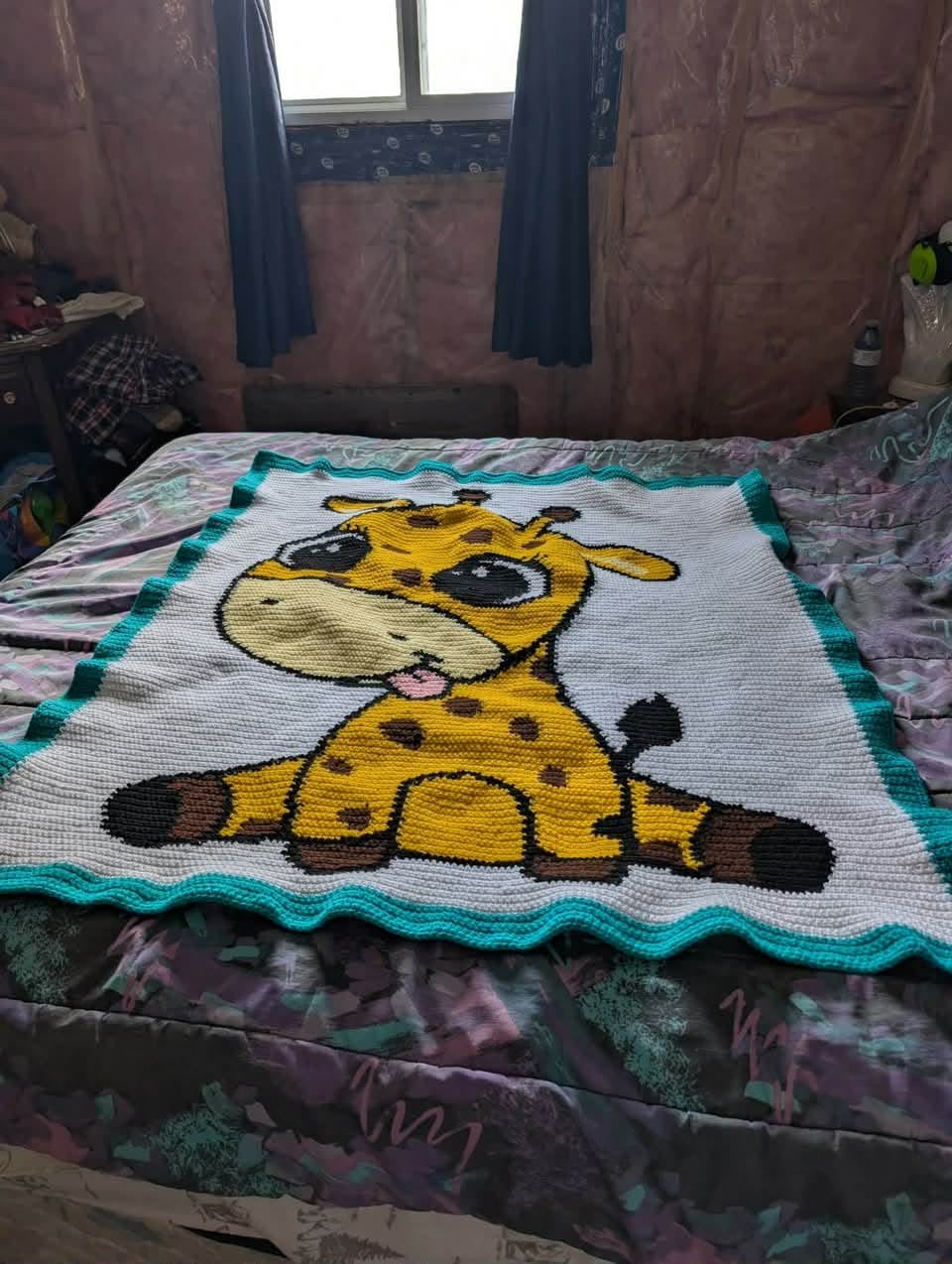 Crocheted blanket with a giraffe design on a bed in a room. Crocheted by MAry Ellen Gauthier