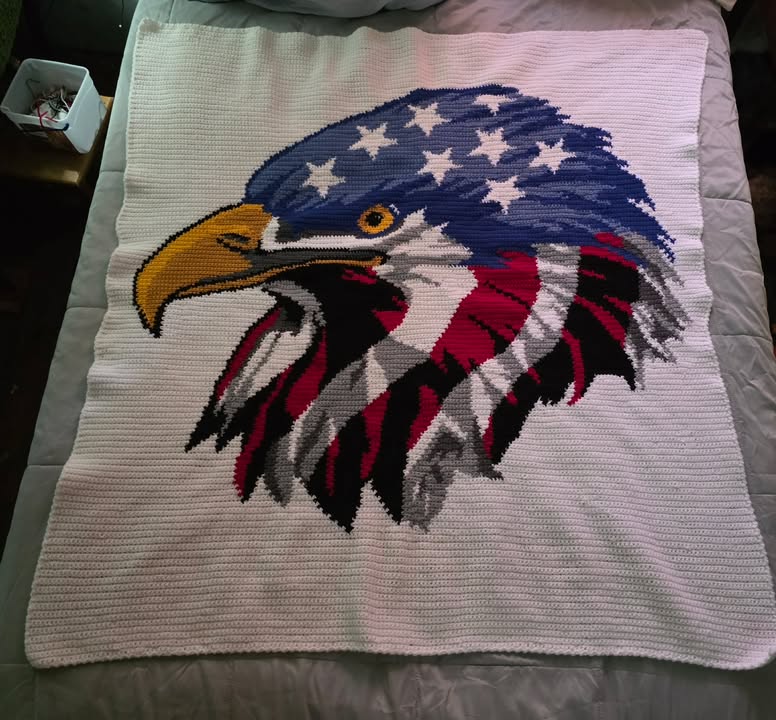 Crocheted blanket with an eagle design featuring the American flag on a bed. Design by Geeky Graphghans. Crochet by Martha Smith Atkins