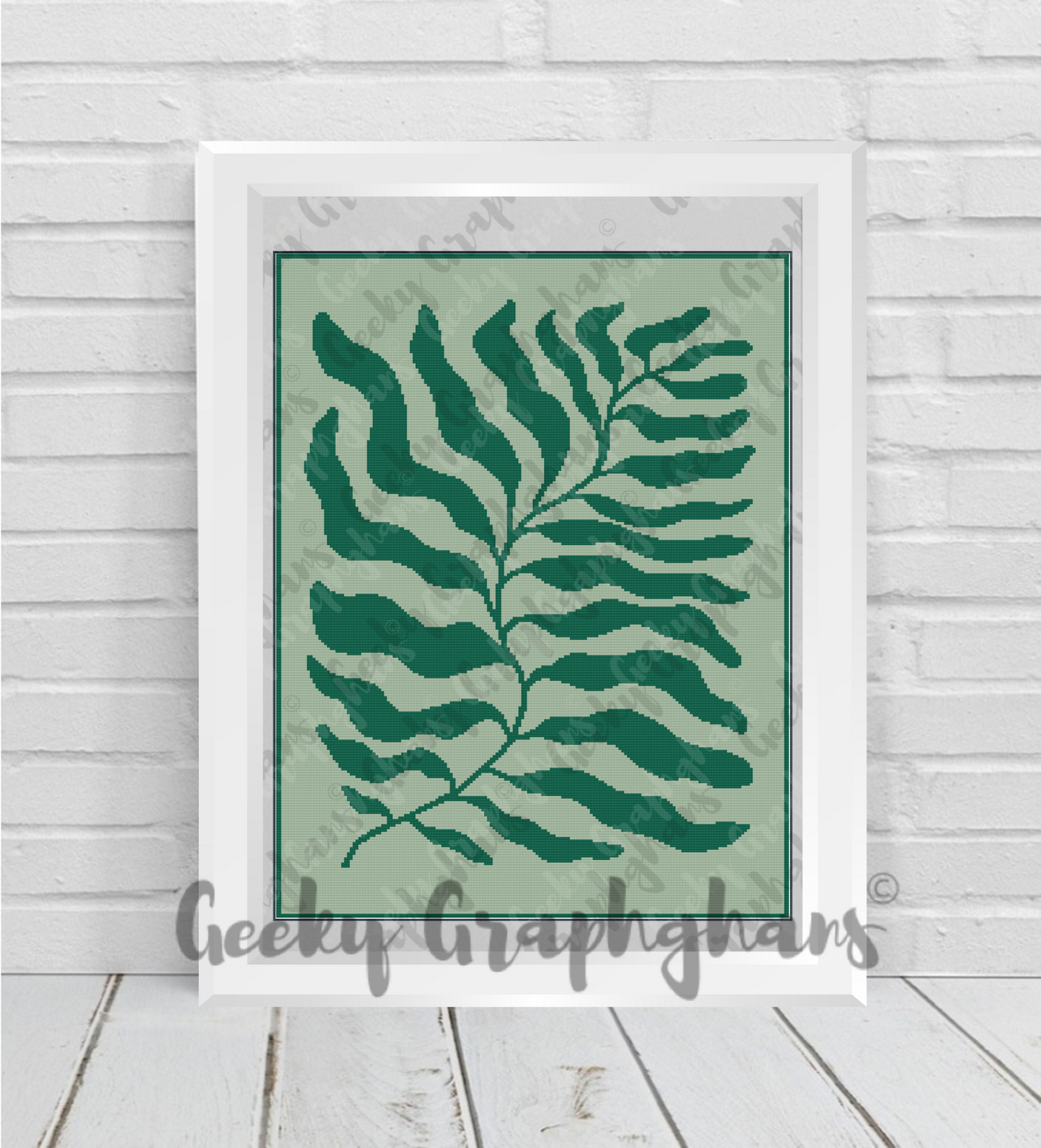 Framed artwork with a green leaf design on a light green background, displayed on a wooden floor.
