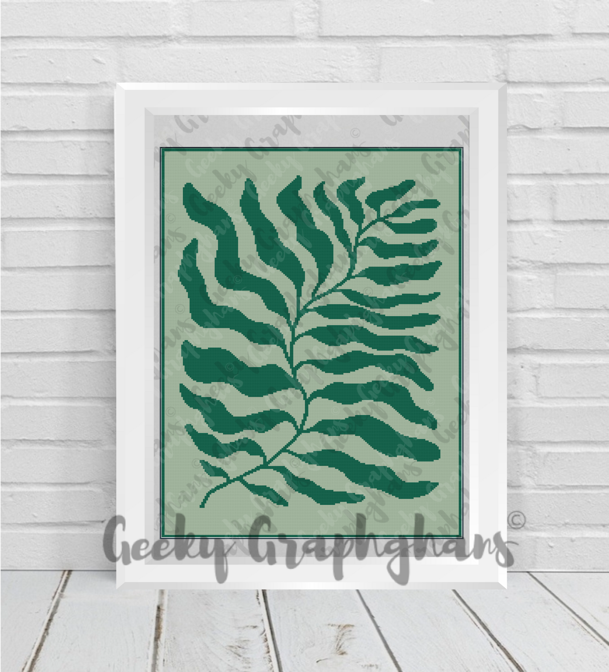 Framed artwork with a green leaf design on a light green background, displayed on a wooden floor.
