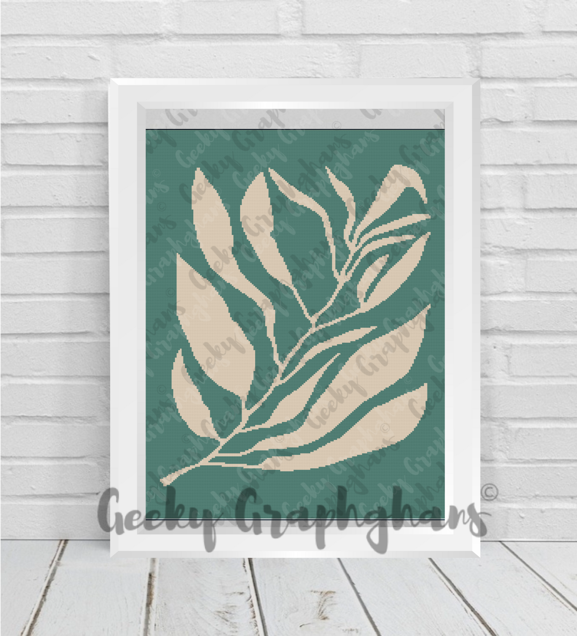 Framed artwork with leaf design on a teal background, displayed on a wooden floor.