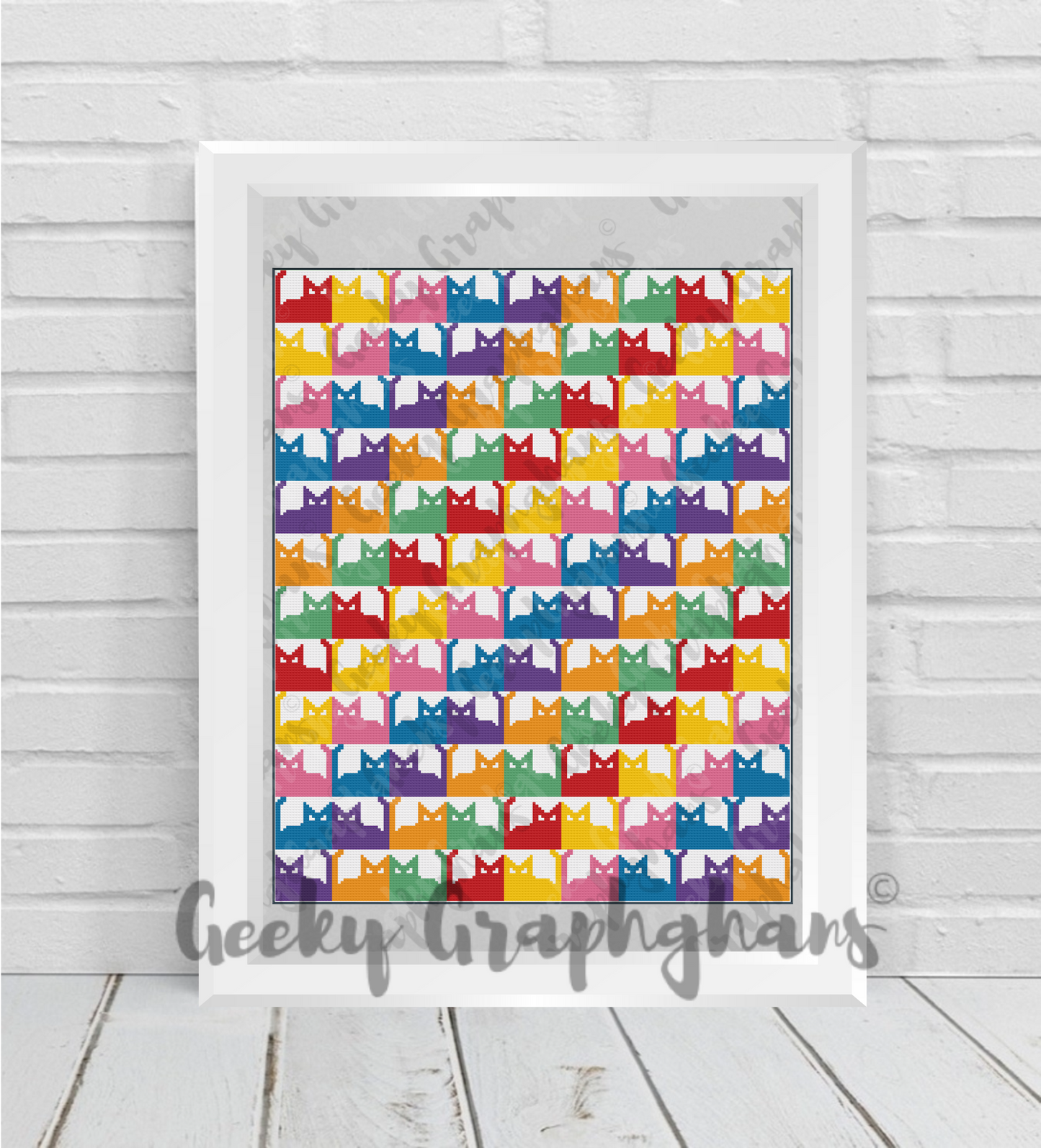 Framed artwork with colorful cat pattern on a wooden floor. Crochet Graphghan pattern by Geeky Graphghans