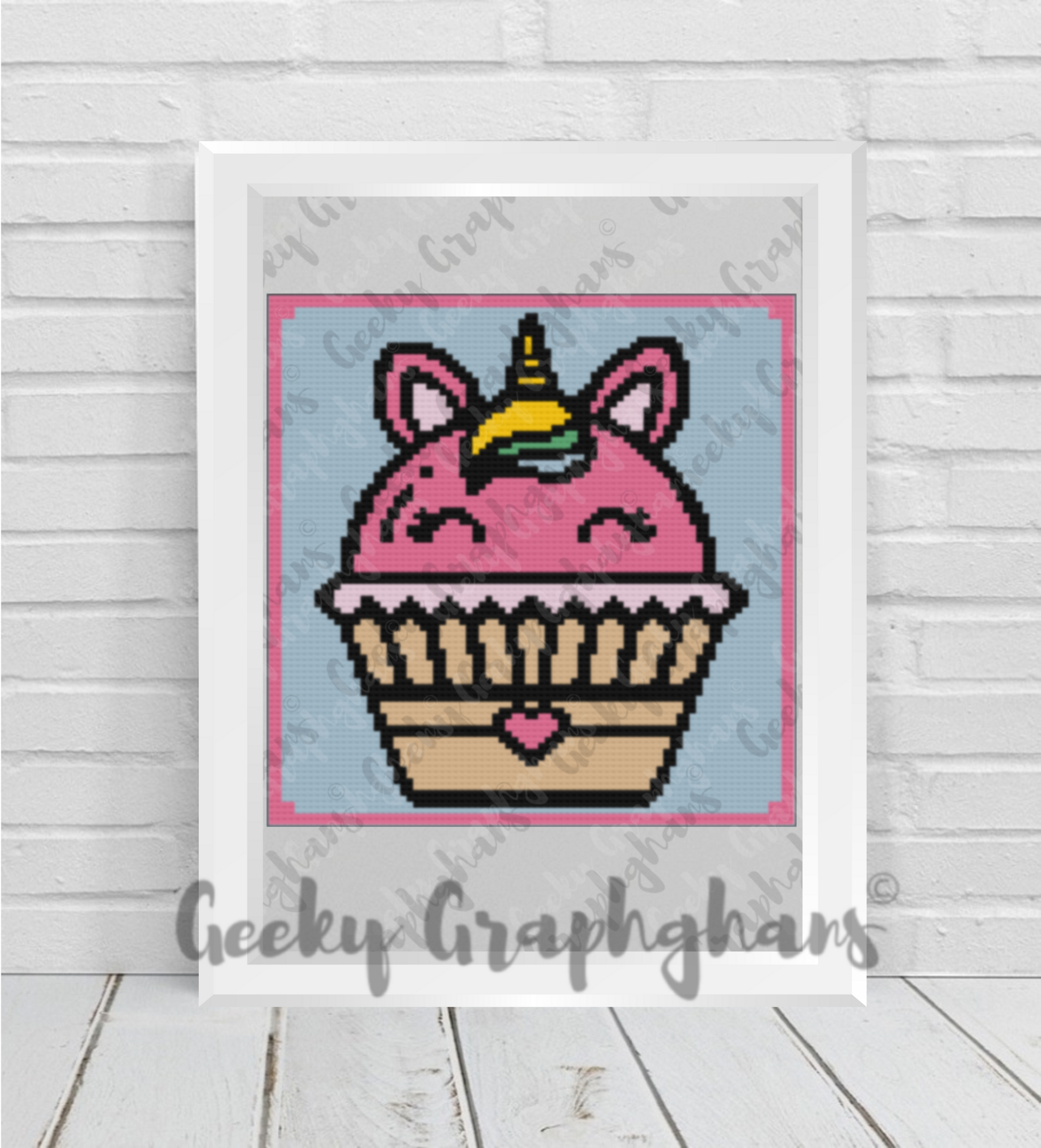 Pixel art of a cupcake with unicorn horns on a wooden surface, framed by 'Geeky Graphghans'.
