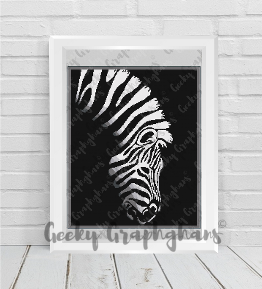 Zebra crochet graphghan pattern. Framed artwork of a zebra's head on a black background, displayed on a wooden floor with a white wall.