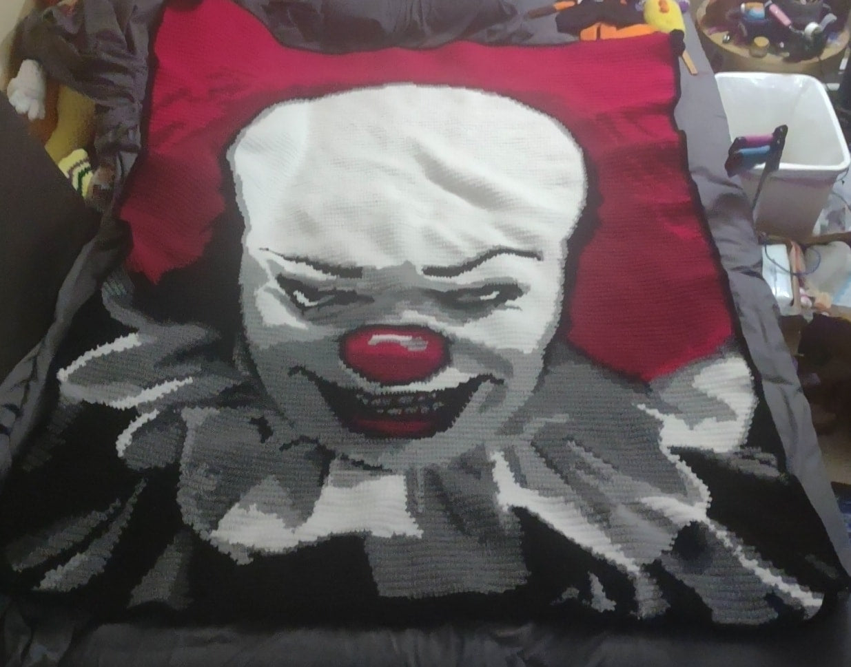 crochet graphghan with a clown design featuring a red nose and gray face on a black background. Pennywise Crochet Graphghan by pattern by Geeky Graphghans. Crocheted by Colburns Creations